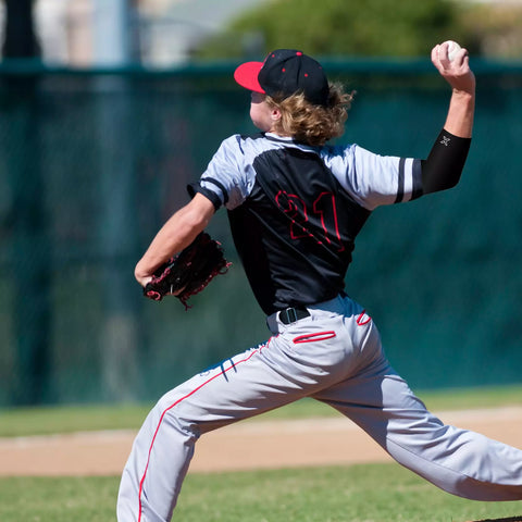 youth baseball pitcher pitching while wearing an elbow compression sleeve for elbow pain